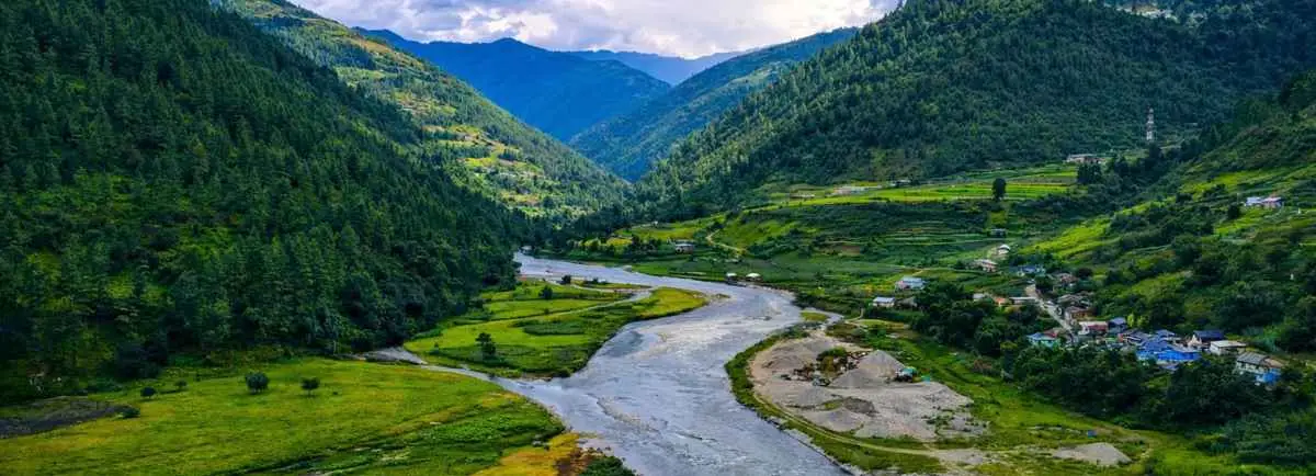 A winding river flowing through a lush green valley surrounded by forested mountains in Sangti.