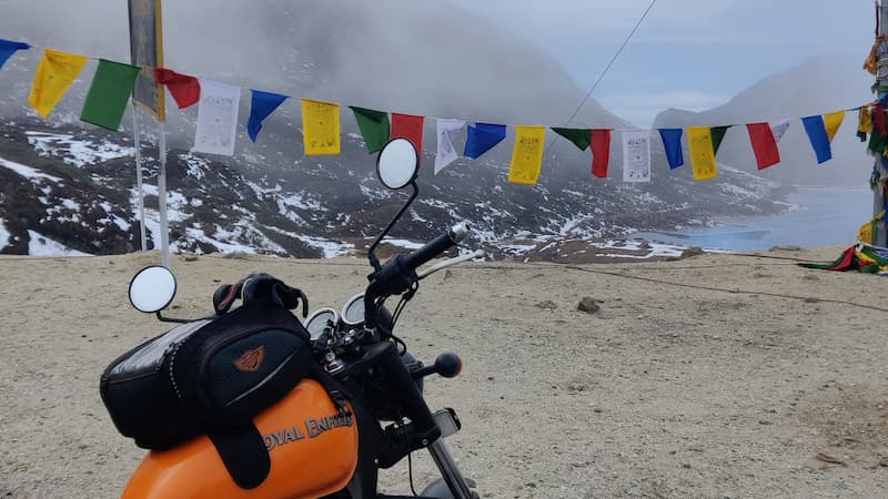 Royal Enfield motorcycle with prayer flags overlooking a misty mountain lake in Arunachal Pradesh