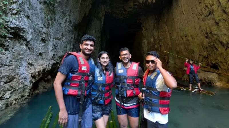 A group of travelers in life jackets pose at the mouth of Krem Chympe cave before bamboo rafting in.