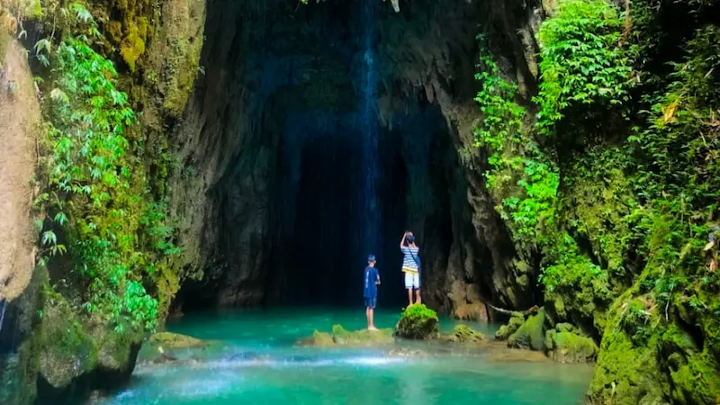 Inside Krem Chympe cave, a natural waterfall drips down the limestone chamber above a turquoise pool.