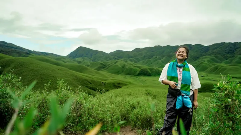 A traveler standing in the green valley at Dzukou, mist rolling over the surrounding hills.