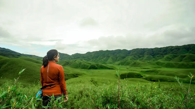 A traveler in an Outdoor Backpacker jacket looking out over the rolling hills of Dzukou Valley.