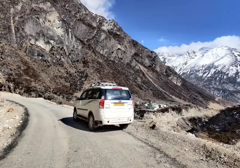 A private vehicle on the winding mountain road through North Sikkim, snow-capped peaks in the distance.