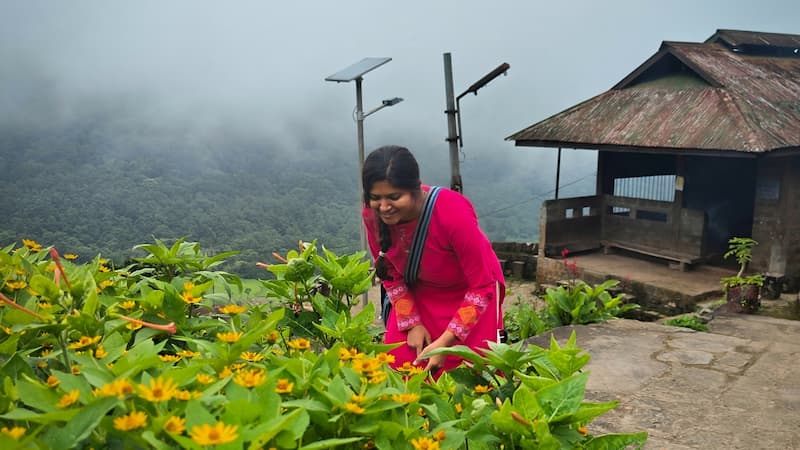 A traveler admiring yellow wildflowers on a misty hilltop viewpoint in Khonoma village, Nagaland